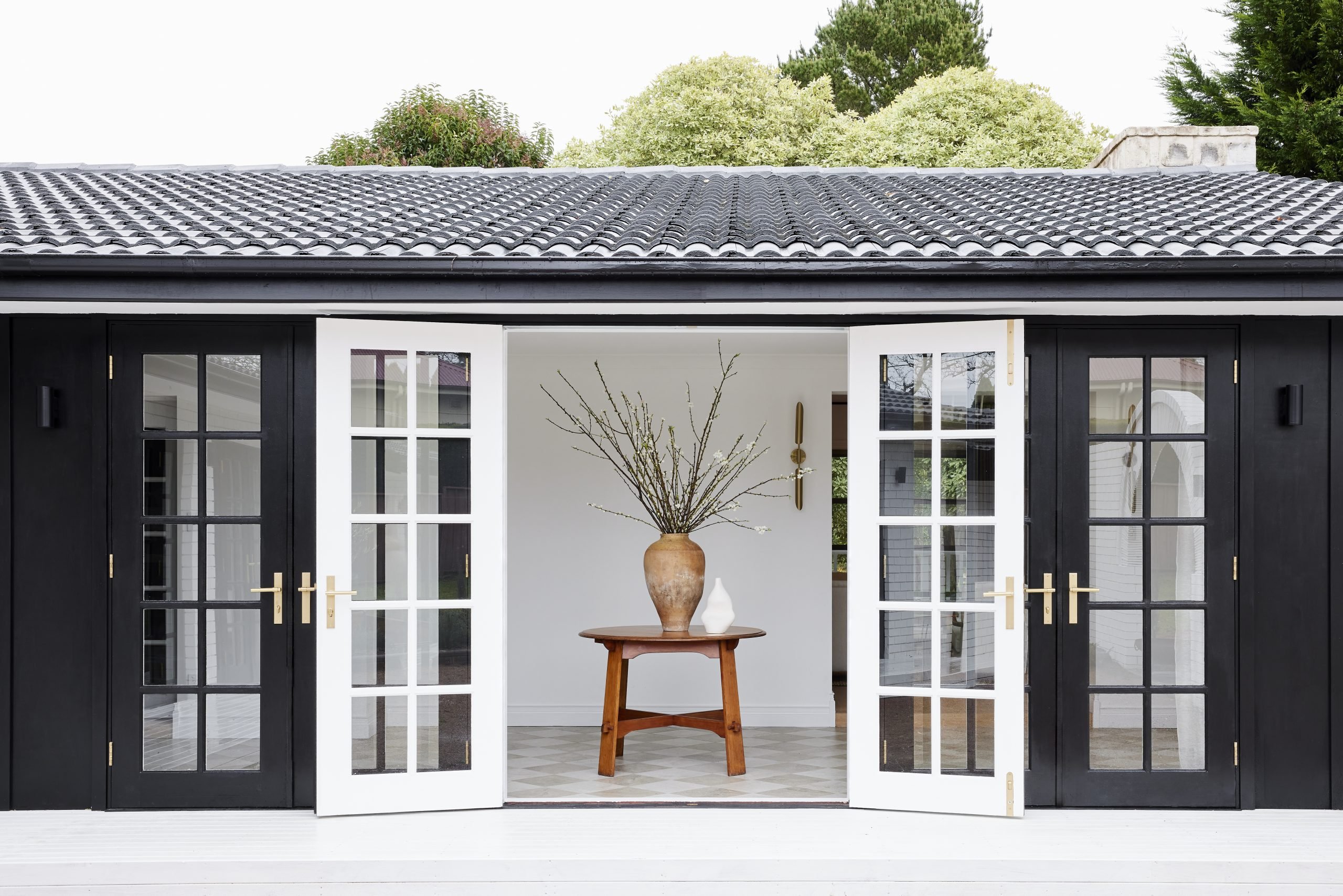 Exterior black and white doors feature the Helsinki Lever on Rectangle Backplate in Brushed Brass