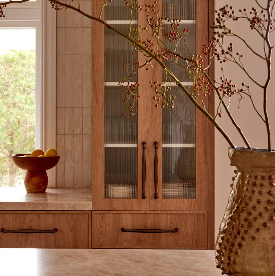 Detail of custom timber joinery with reeded glass doors and dark pull handles, softened by natural light and botanical styling.
