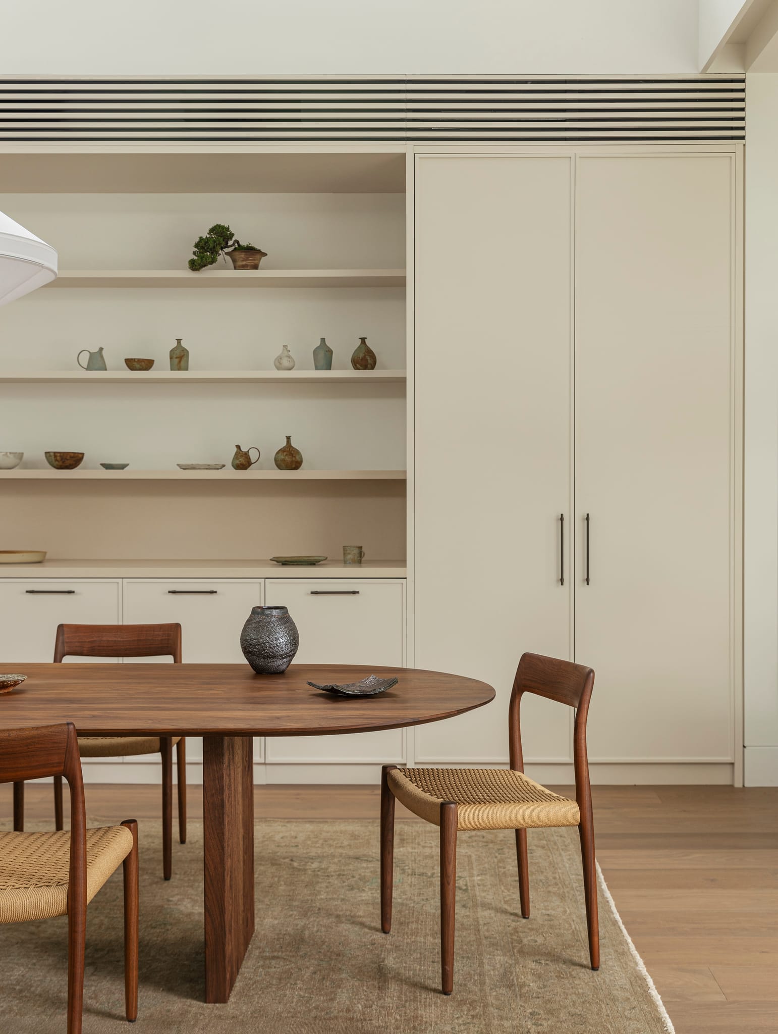 Warm dining space featuring a timber table, woven-seat chairs, and cream cabinetry with slim pull handles.