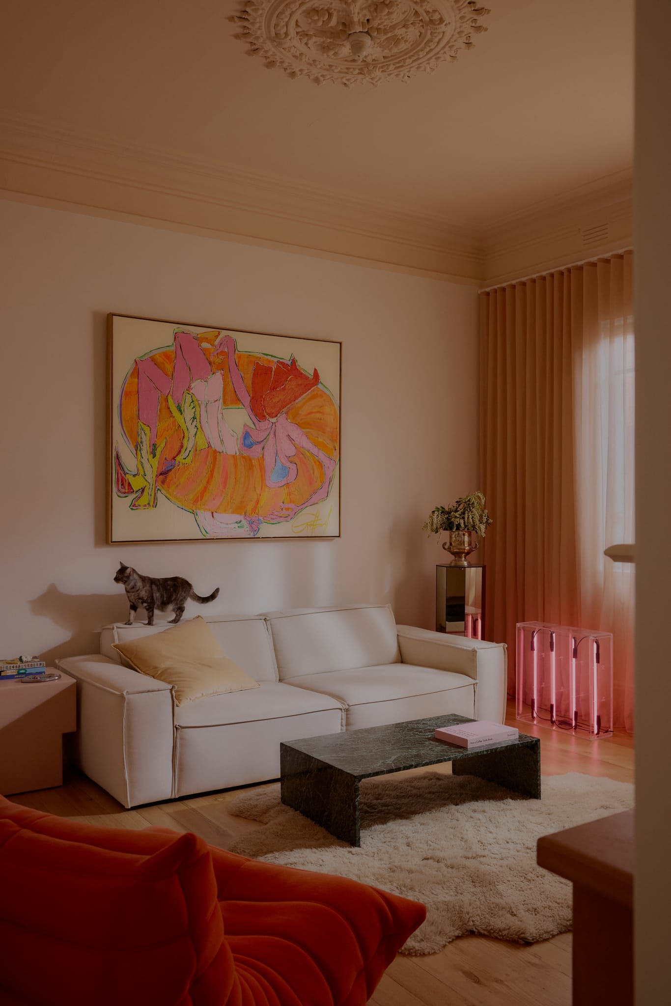 Warm living space featuring a cream sofa, abstract artwork, soft pink furnishings, and sheer curtains.